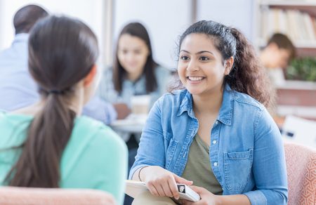 Female student with binder talking with a peer in a lounge area