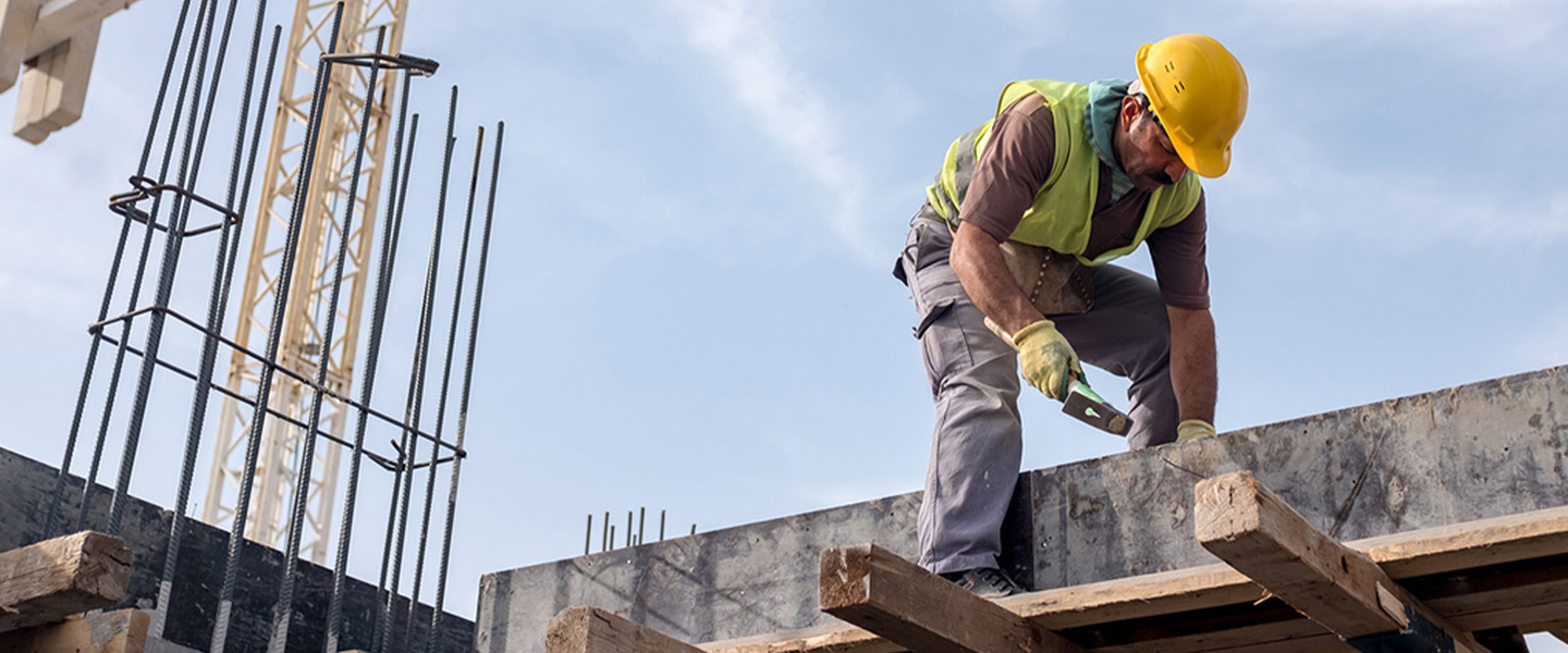 Construction worker hammers while standing on concrete and wooden beams