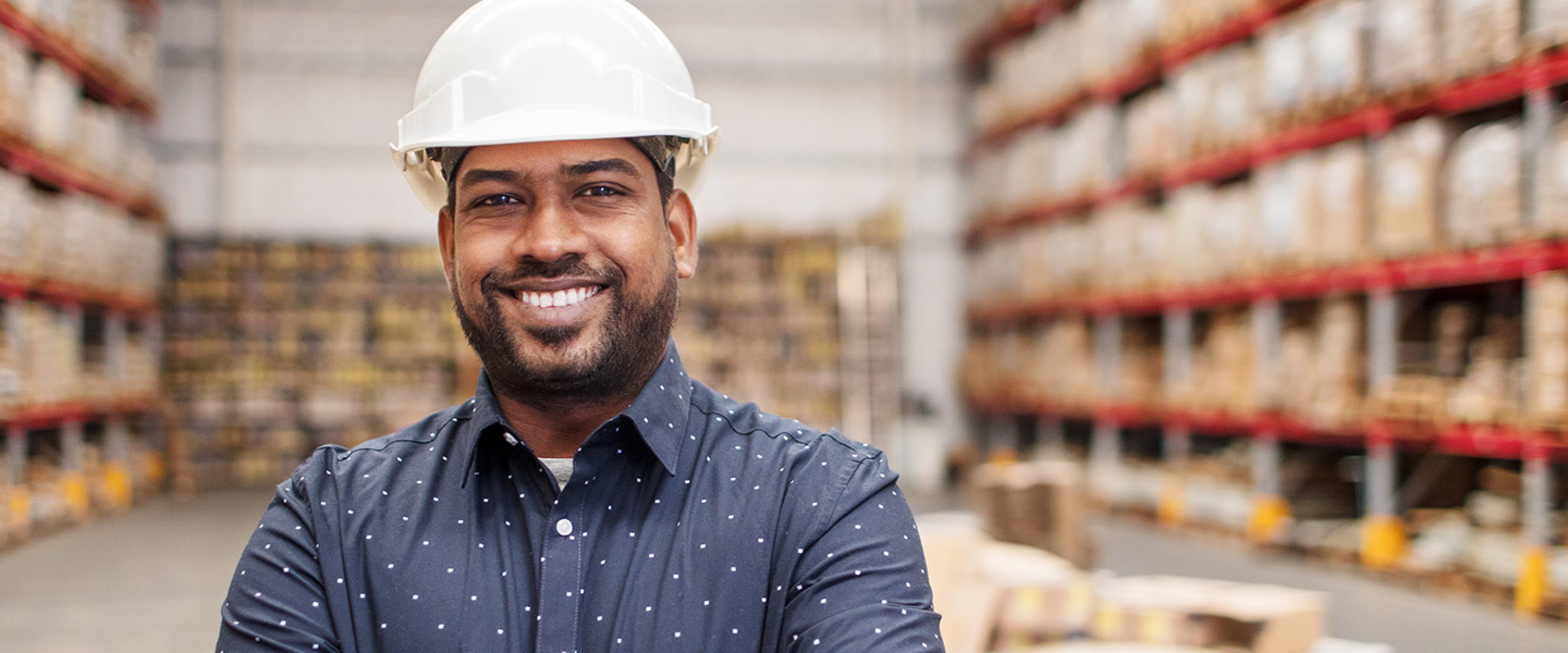Man wearing hard hat smiles in a warehouse
