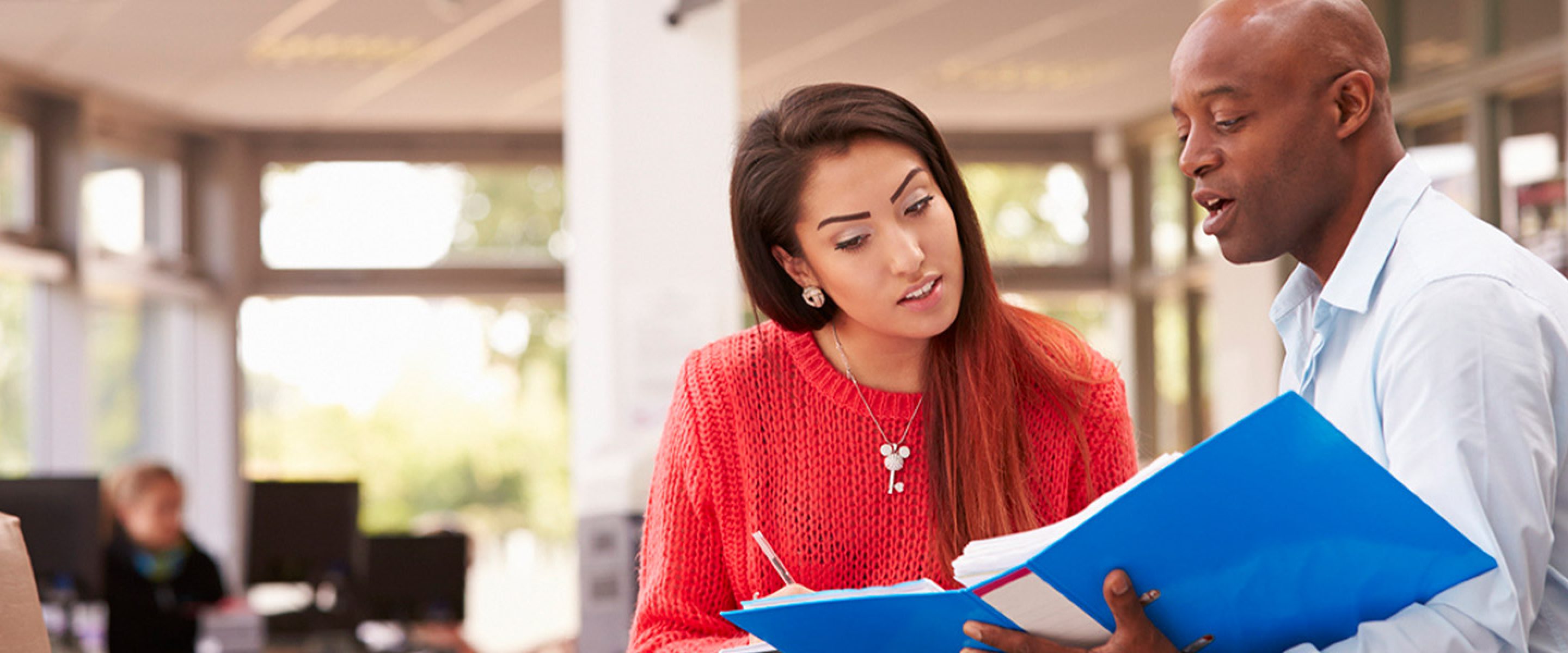 Male counselor and female student look at a blue binder together