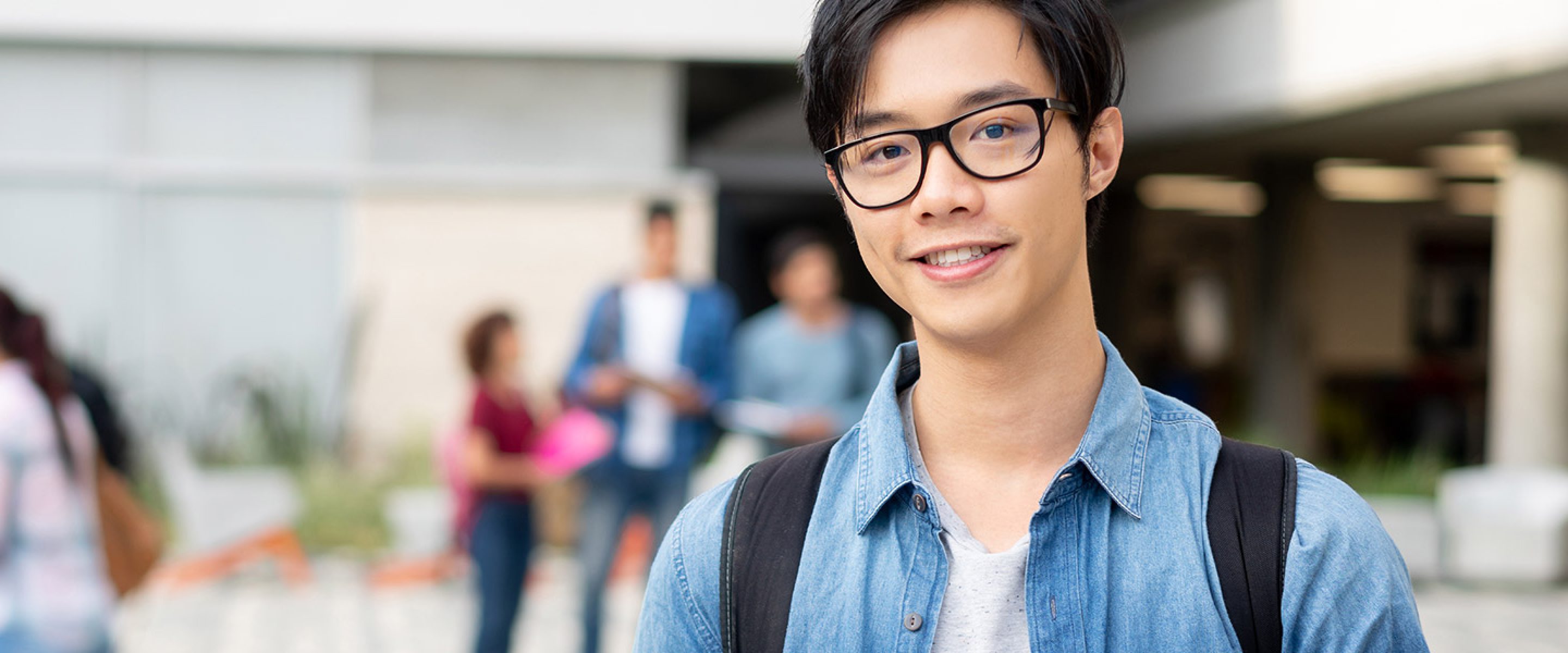 Young Asian male student poses in front of school quad area
