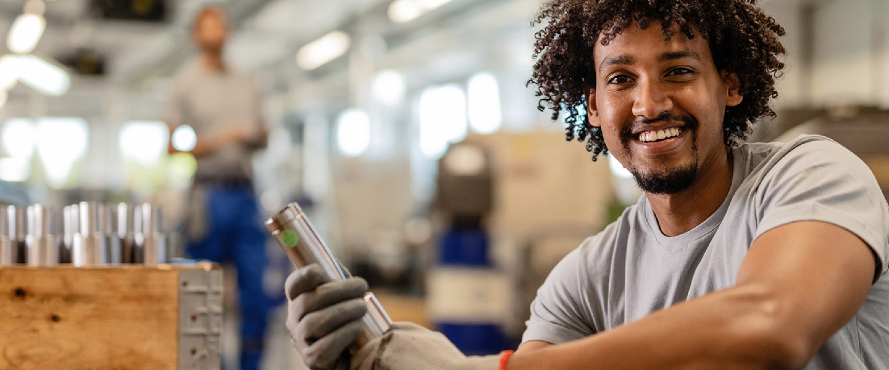 Young worker smiles in workshop area while holding a mechanical part