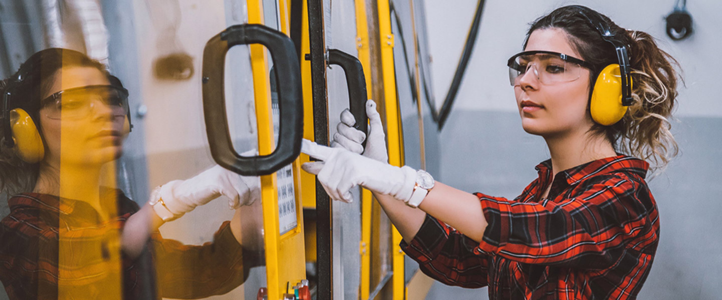 Young female worker wearing hearing protection opens machinery doors